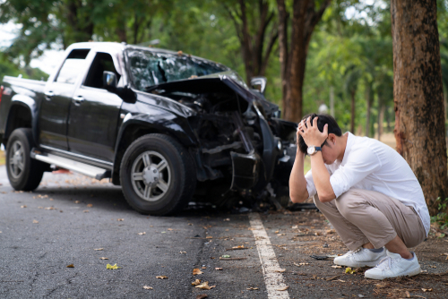 A man sitting on the roadside with his head in his hands after a car crash with a damaged black pickup truck.