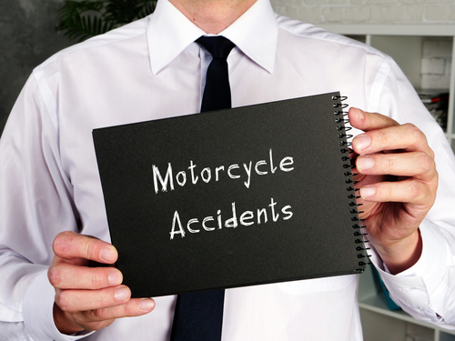 Person in a white shirt and dark tie holding a black notebook labeled Motorcycle Accidents.