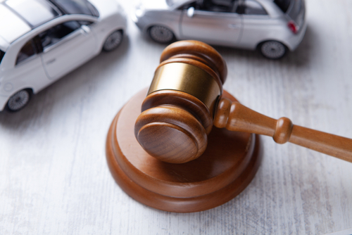 Wooden judge’s gavel resting on a white table beside two small model cars, representing a car accident legal case.