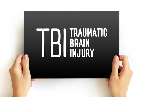 Hands holding a black sign with the white text TBI Traumatic Brain Injury, representing awareness and legal support for brain injury victims