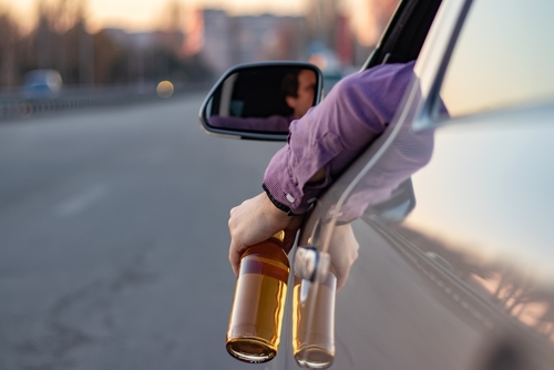 Person holding two beer bottles out of a car window while driving.