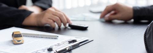 Close-up of two people discussing a car accident claim at a desk with paperwork, pens, and a small toy car.