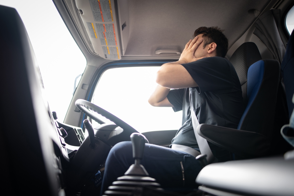 Tired truck driver sitting in cab covering face with hands