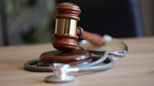 Close-up of a wooden judge gavel resting on a stethoscope on a desk, symbolizing medical malpractice or healthcare law.