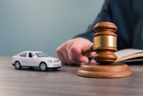 Judge’s gavel next to a white toy car on a desk, symbolizing a car accident lawsuit or legal decision.
