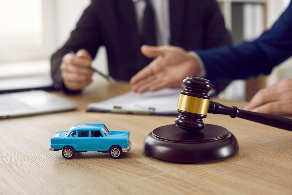 Judge’s gavel on a desk with a toy car and two people discussing in the background.