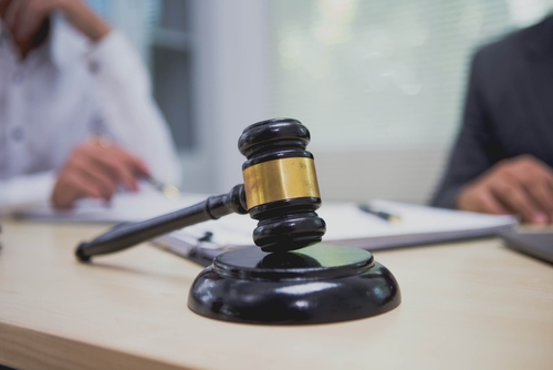 A judge’s gavel resting on a wooden desk with people in the background.