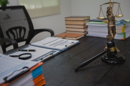 A lawyer’s desk with legal documents, contract folder, gavel, magnifying glass, and the scales of justice.