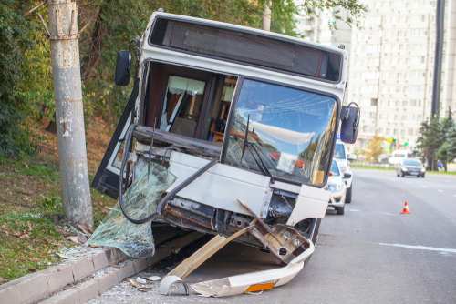 City bus crashed into a pole on a street with smashed windows and bent frame, indicating a major collision in an urban area.