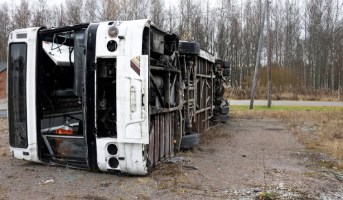 Overturned bus lying on its side after a serious road accident, showing severe exterior damage and debris scattered around.