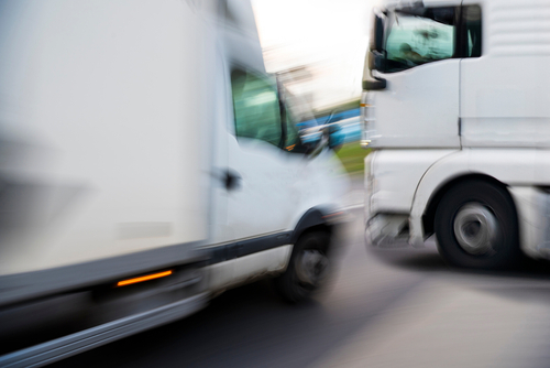 Two white trucks narrowly avoiding a collision on the road, captured with motion blur.