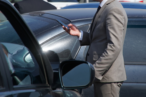 man in a gray business suit stands between parked cars, holding a smartphone and inspecting the scene after a car accident.