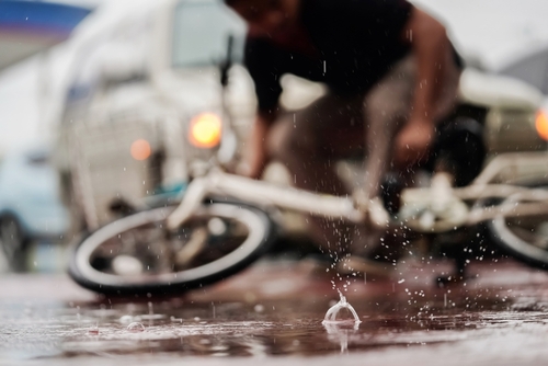 Cyclist falling on a wet road during heavy rain in front of a blurred truck, showing motion and danger from slick conditions.