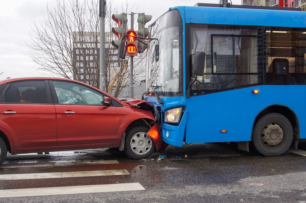 A red car and a blue bus after a head-on collision at a traffic light, with airbags deployed and visible front-end damage.