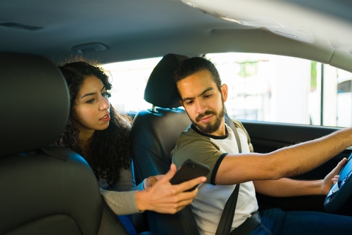 A female passenger showing her phone screen to a male rideshare driver inside a car during a trip.