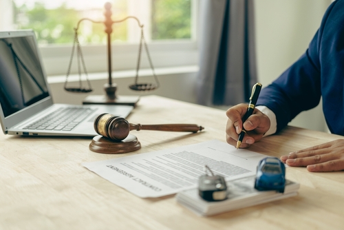 A lawyer signing legal documents beside a gavel, car keys, and a miniature car on a desk, symbolizing car accident claims.