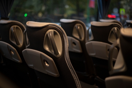 Rows of modern bus seats with built-in handles, viewed from the aisle under dim lighting.