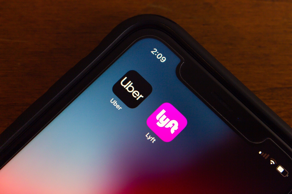 A close-up of a smartphone displaying Uber and Lyft app icons on the home screen, representing rideshare services.