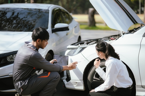 Mechanic inspecting front-end collision damage while explaining details to car owner outdoors