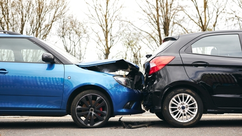 A rear-end collision between a blue car and a black car on a road, showing visible front-end and rear-end damage.