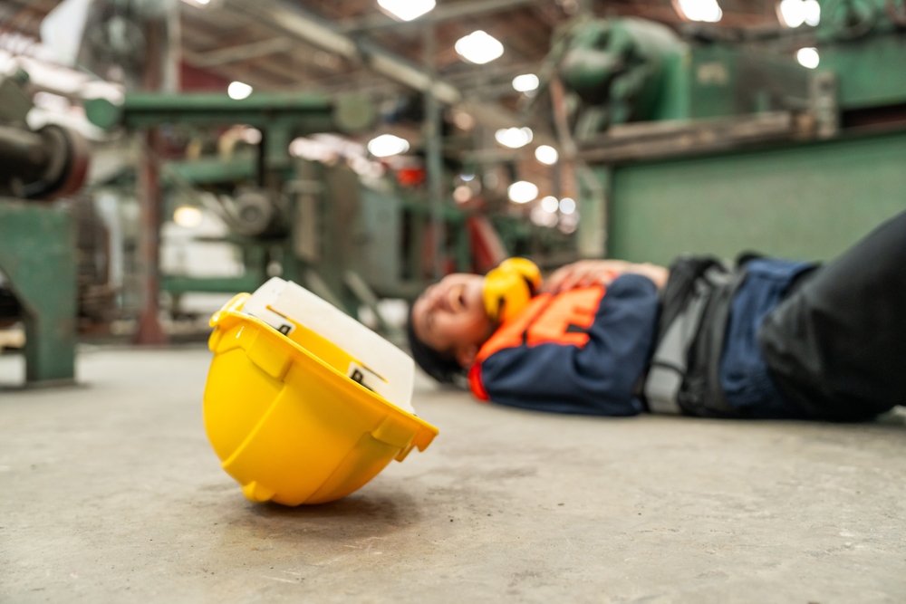construction worker lying on factory floor after workplace injury with hard hat in foreground