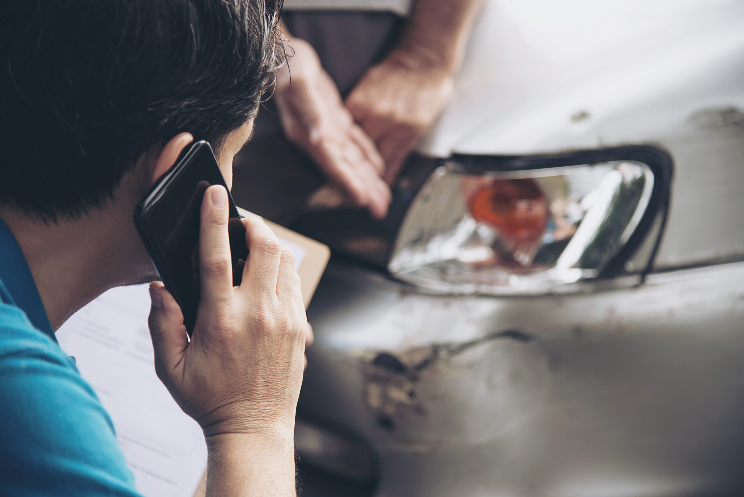 Man on phone documenting vehicle damage for uninsured driver accident insurance claim