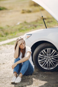 Woman sitting beside broken down car looking stressed after uninsured driver accident